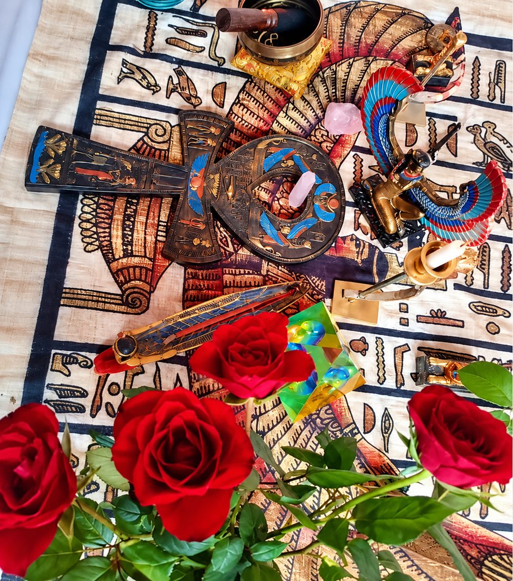 Altar sobre um tecido egípcio, com um ankh, a estátua de Ísis alada, uma tigela, uma vela e rosas vermelhas