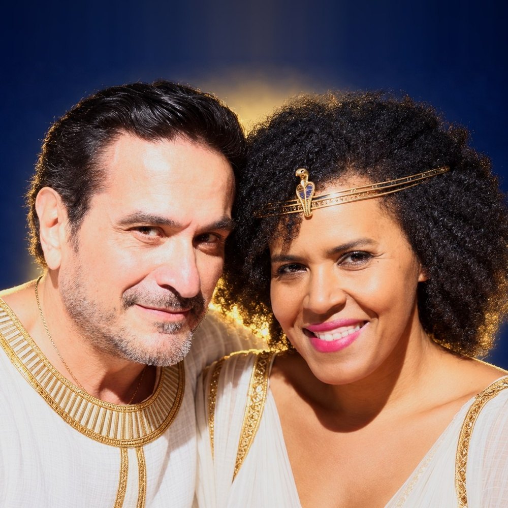 Ayala e Ayam, lado a lado, vestidos de branco e dourado, ela com um diadema de serpente